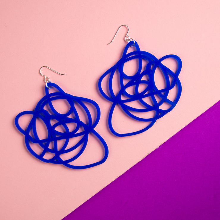 blue statement earrings over pale pink and purple background