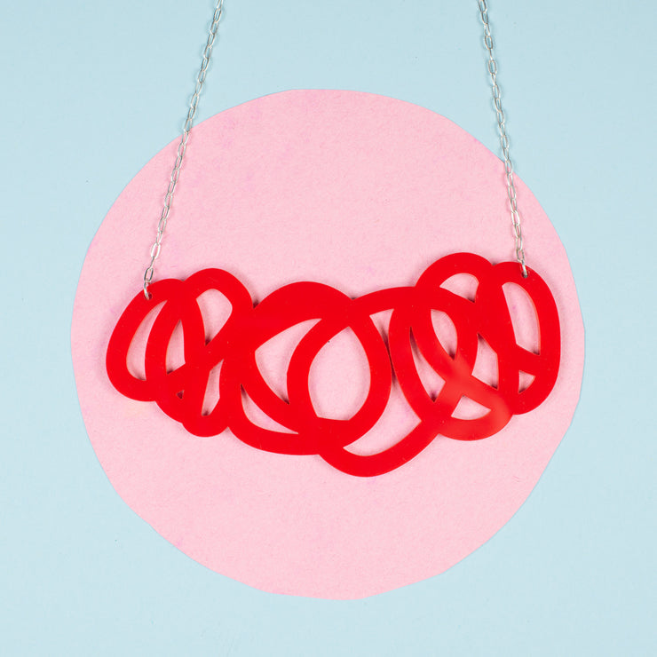 chunky red statement necklace shown over pink and blue background
