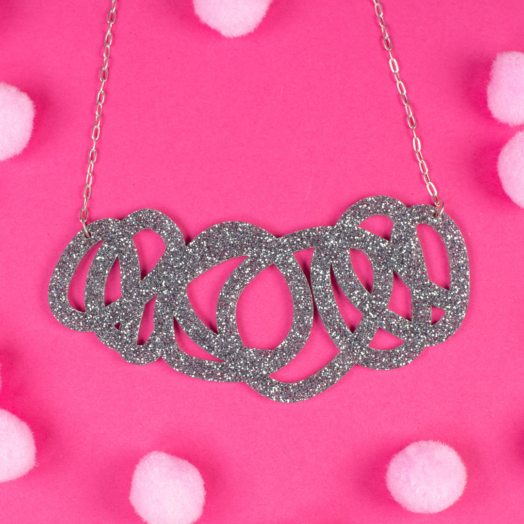Chunky silver glitter statement necklace on pink background