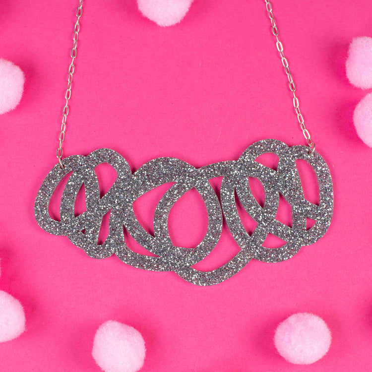 Chunky silver glitter statement necklace on pink background