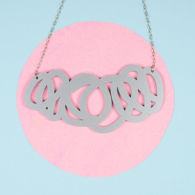 Chunky silver statement necklace on pink and blue background