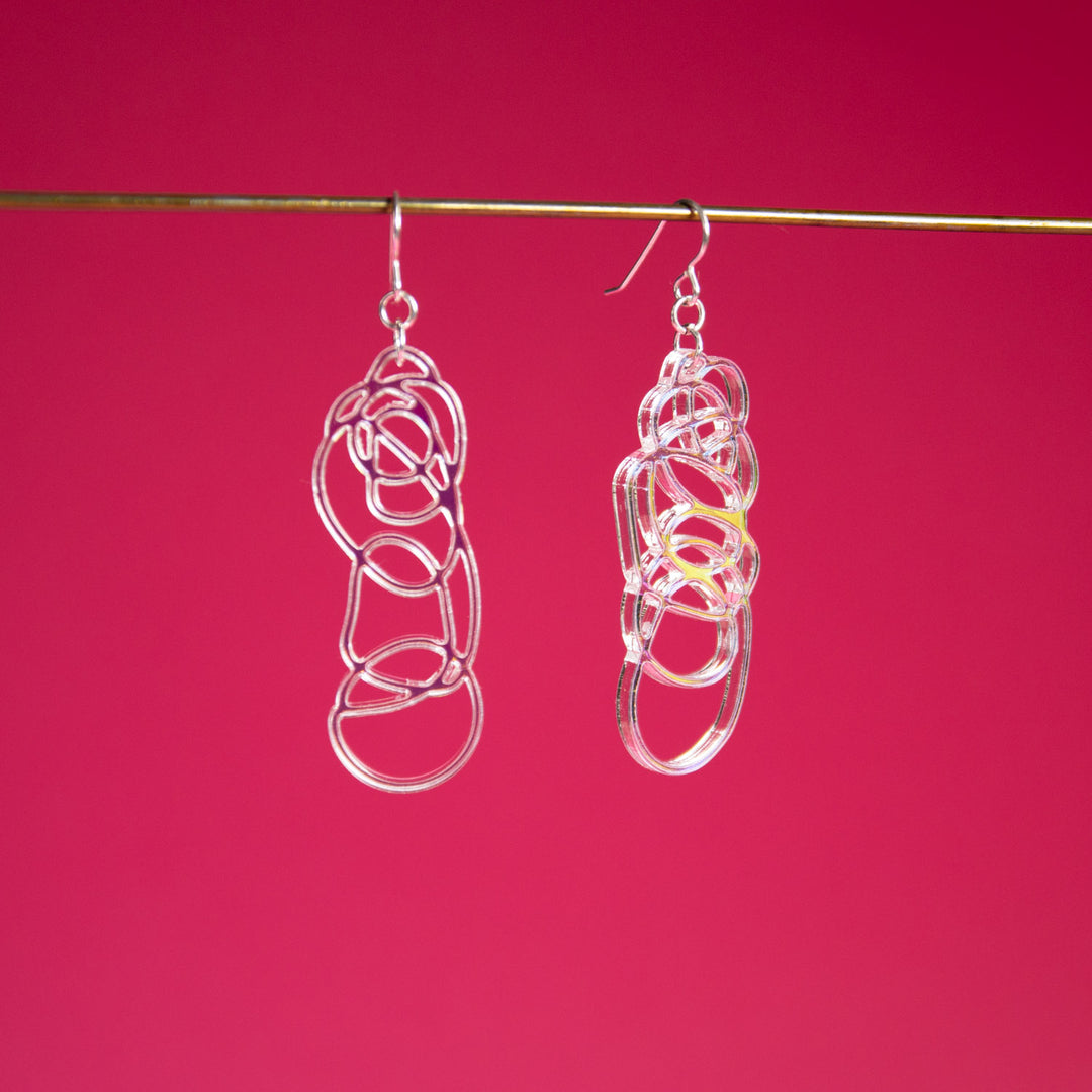 Iridescent dangle earrings shown over pink background