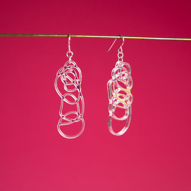 Iridescent dangle earrings shown over pink background