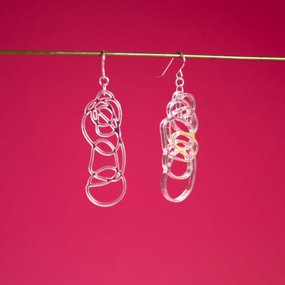 Iridescent dangle earrings shown over pink background