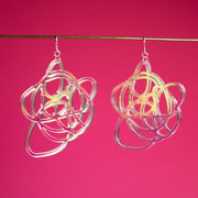 Iridescent graffiti earrings shown hanging from brass rod in front of a pink backdrop