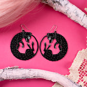 Large black dog earrings on pink background