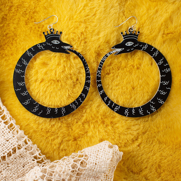 large black ouroboros earrings over yellow faux fur