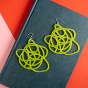 lime green statement earrings lying on a dark blue book