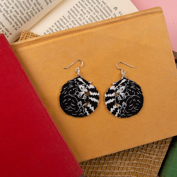 black and white raccoon earrings atop book