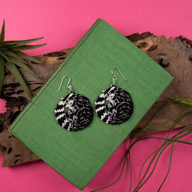 black and white raccoon earrings on top of green book