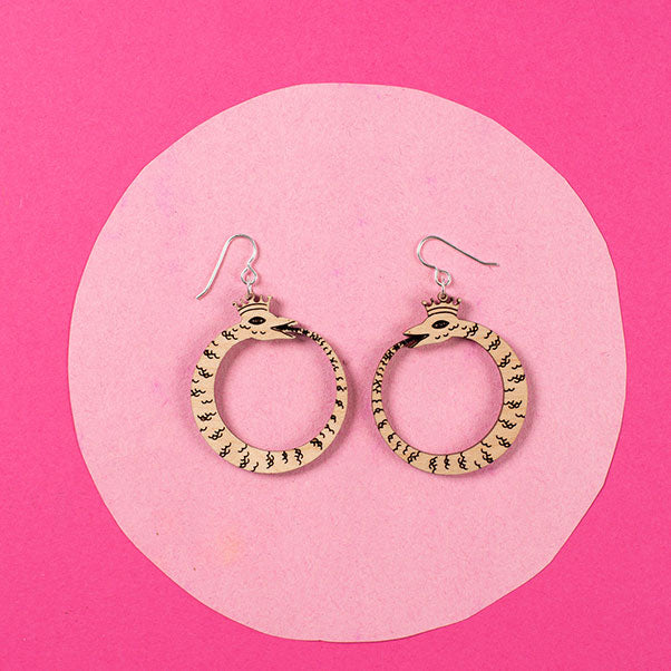 small wood ouroboros earrings styled over pink background