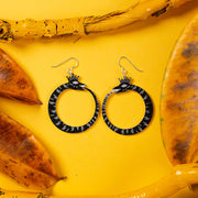 small black ouroboros earrings on yellow background