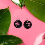 small black wolf earrings on pink background with green leaves