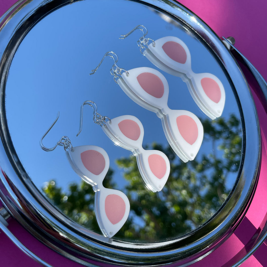 Small and Large White sunglass earrings shown lying on a mirror