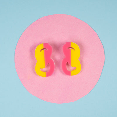 Pink and yellow statement stud earrings on pink and blue background